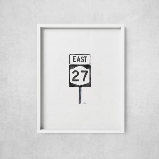 Framed artwork of a road sign with 'East 27' on a gray wall