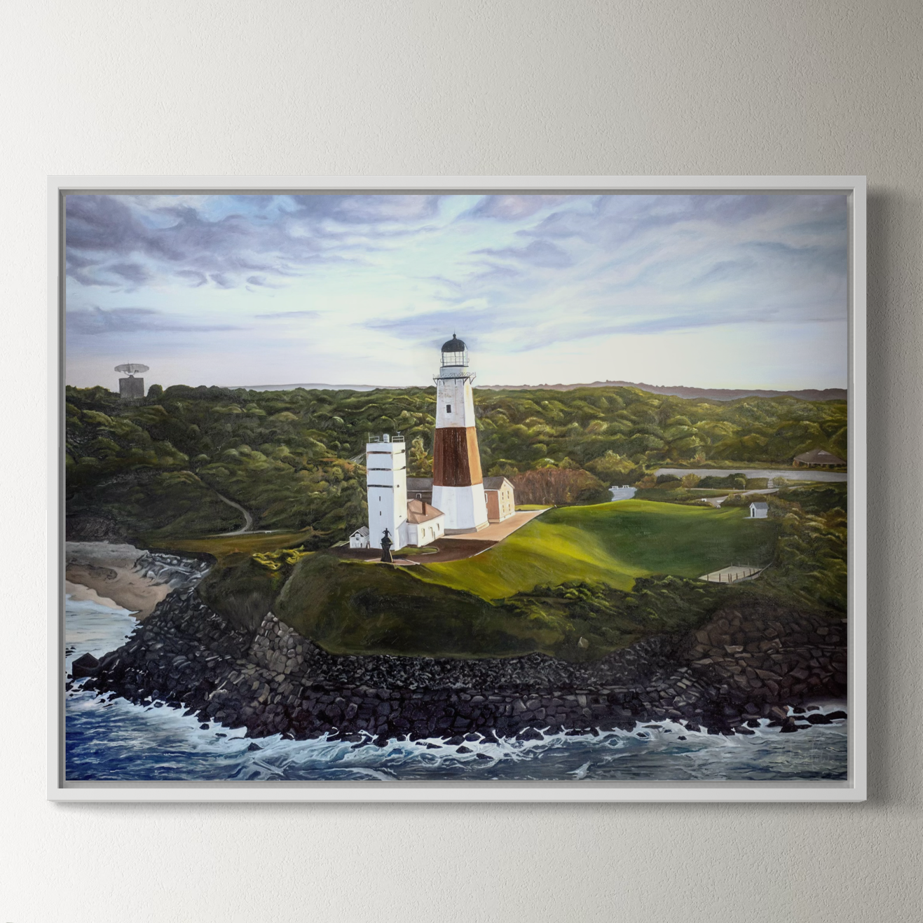 Framed painting of a lighthouse on a rocky outcrop with ocean and landscape in the background.
