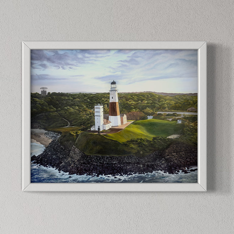 Framed artwork of a lighthouse on a cliff with a body of water and green landscape.