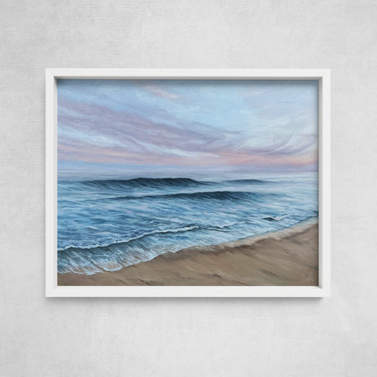 A framed print of a beach scene with waves rolling onto the shore, set against a pink and blue pastel sky.