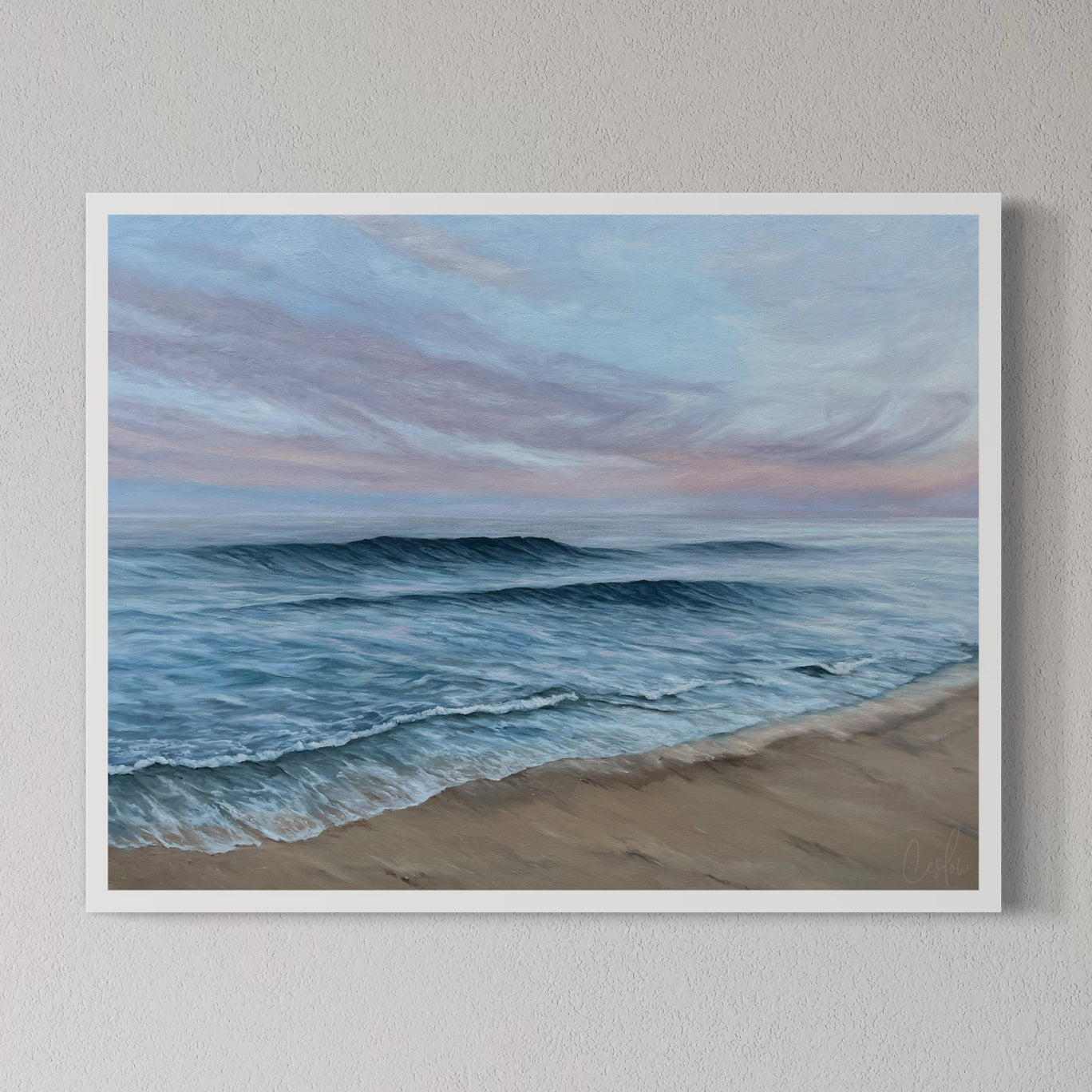 A framed print of a beach scene with waves rolling onto the shore, set against a pink and blue pastel sky.