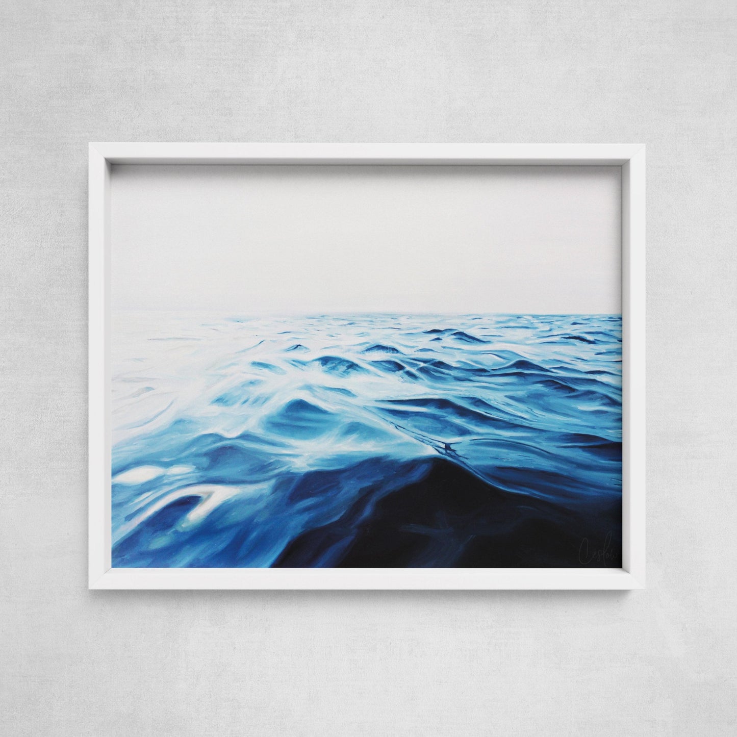 A framed fine art paper print of the ocean horizon, displayed on a wall.