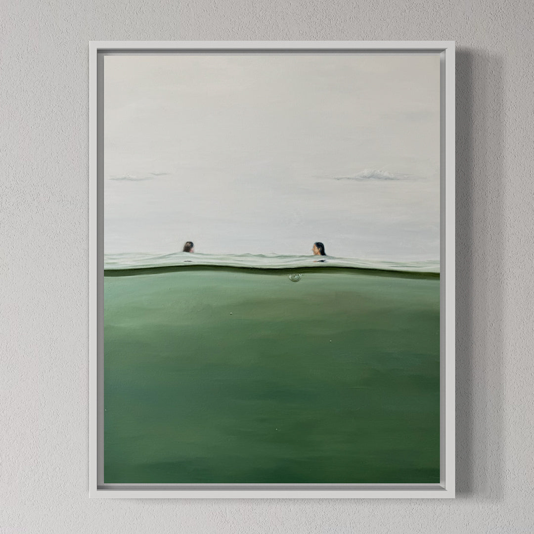 Framed artwork of two people peeking over a green surface with a white frame on a gray wall.
