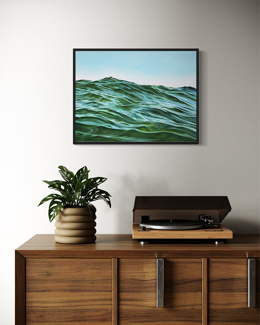 Framed artwork of a wavy green landscape above a wooden cabinet with a plant and record player.