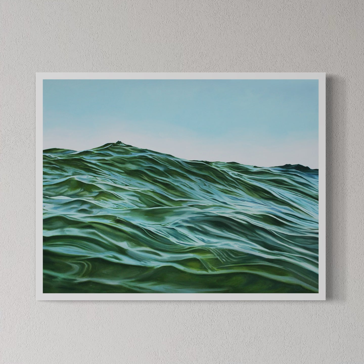 A framed fine art print of a rolling green and blue ocean, with a white frame, displayed on a wall.