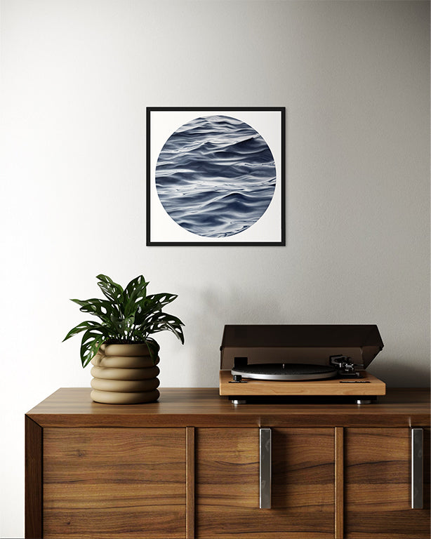 Wooden cabinet with a plant and record player, framed artwork above on a plain wall.