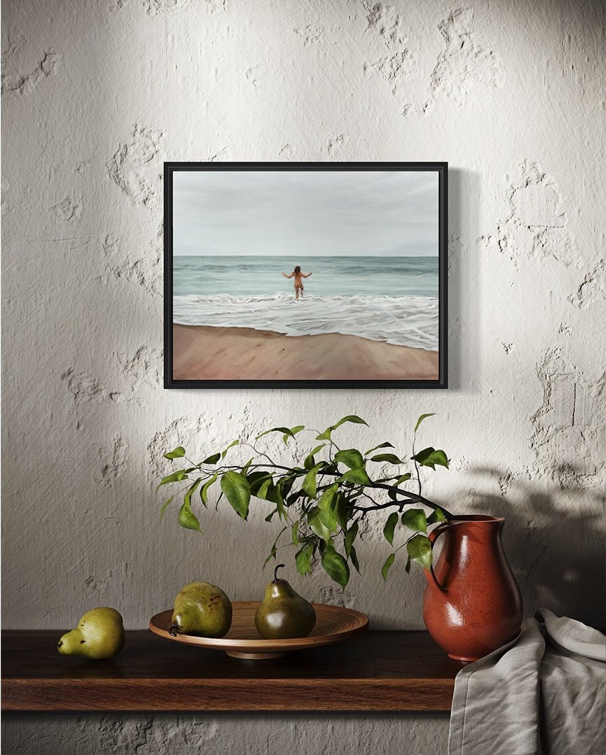 Framed artwork of a person on a beach hanging on a textured wall above a wooden shelf with pears and a pitcher.