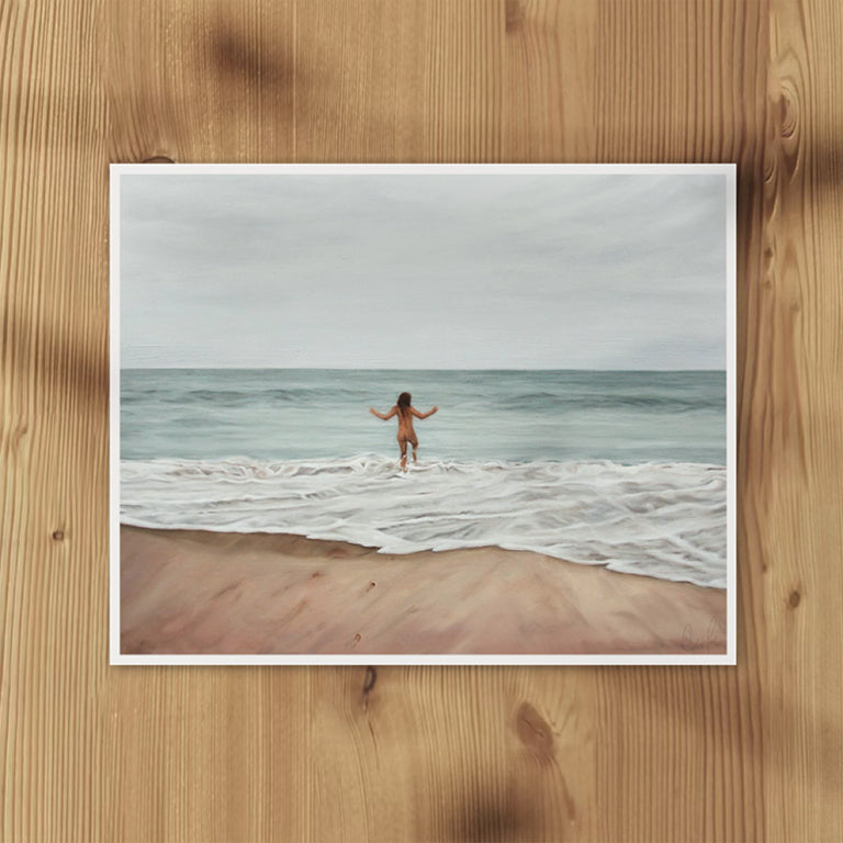 Art print of a person standing on a beach with ocean waves, displayed on a wooden surface.