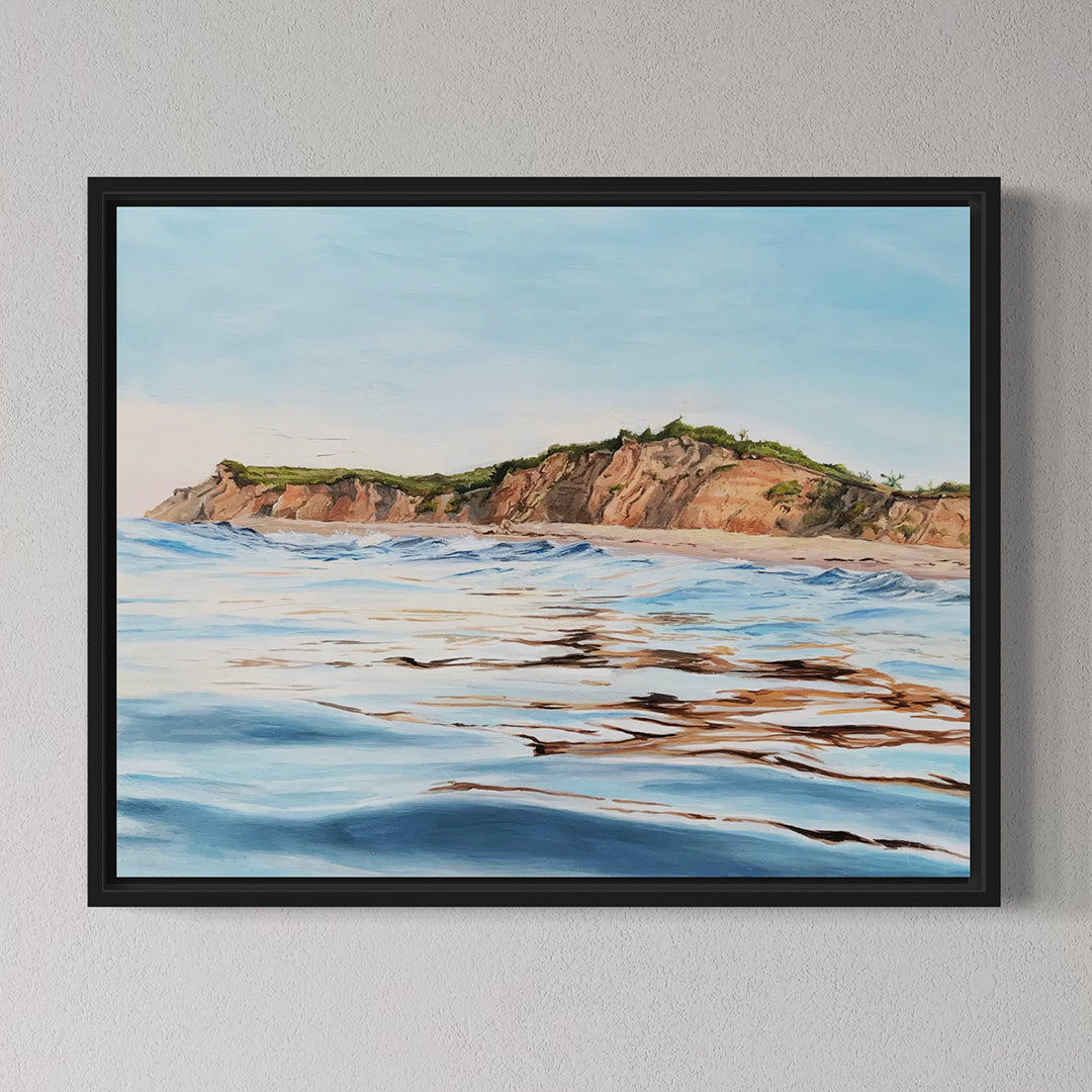 Framed artwork of a coastal landscape with water and cliffs on a gray wall.
