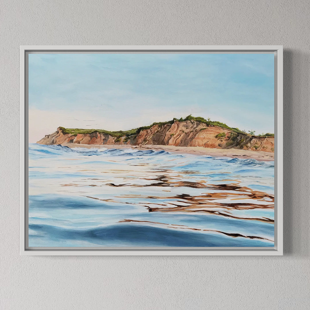 Framed artwork of a coastal landscape with cliffs and ocean waves on a gray wall.