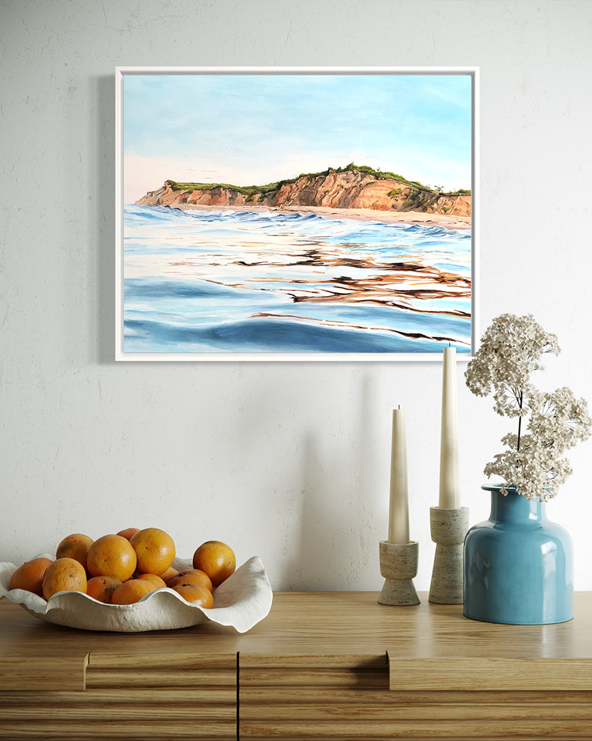 Framed beach artwork on a wall above a wooden console table with decorative items.