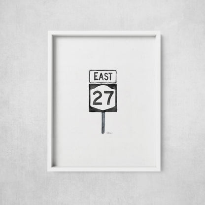 Framed artwork of a road sign with 'East 27' on a gray wall