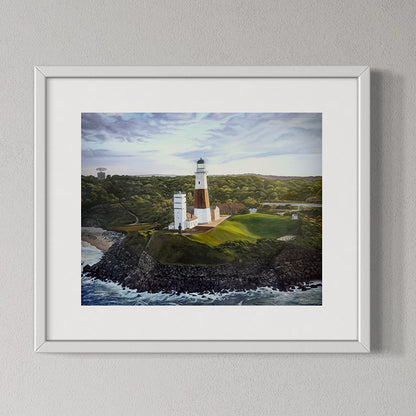 Framed artwork of a lighthouse on a rocky island with a body of water and green landscape.