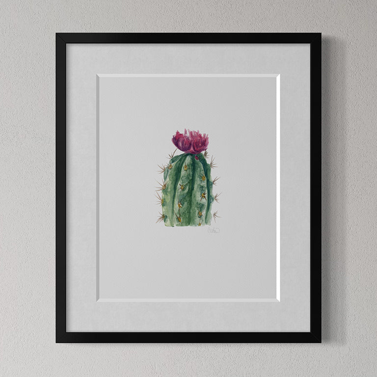 Framed artwork of a cactus with a pink flower on a gray wall.