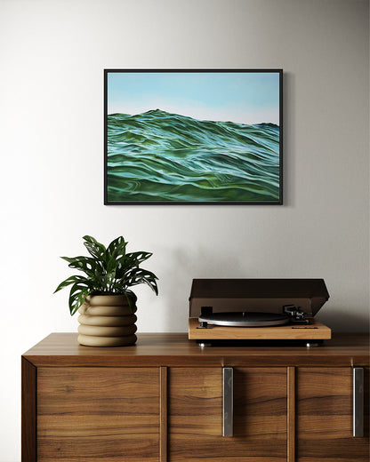 Framed artwork of a wavy green landscape above a wooden cabinet with a plant and record player.