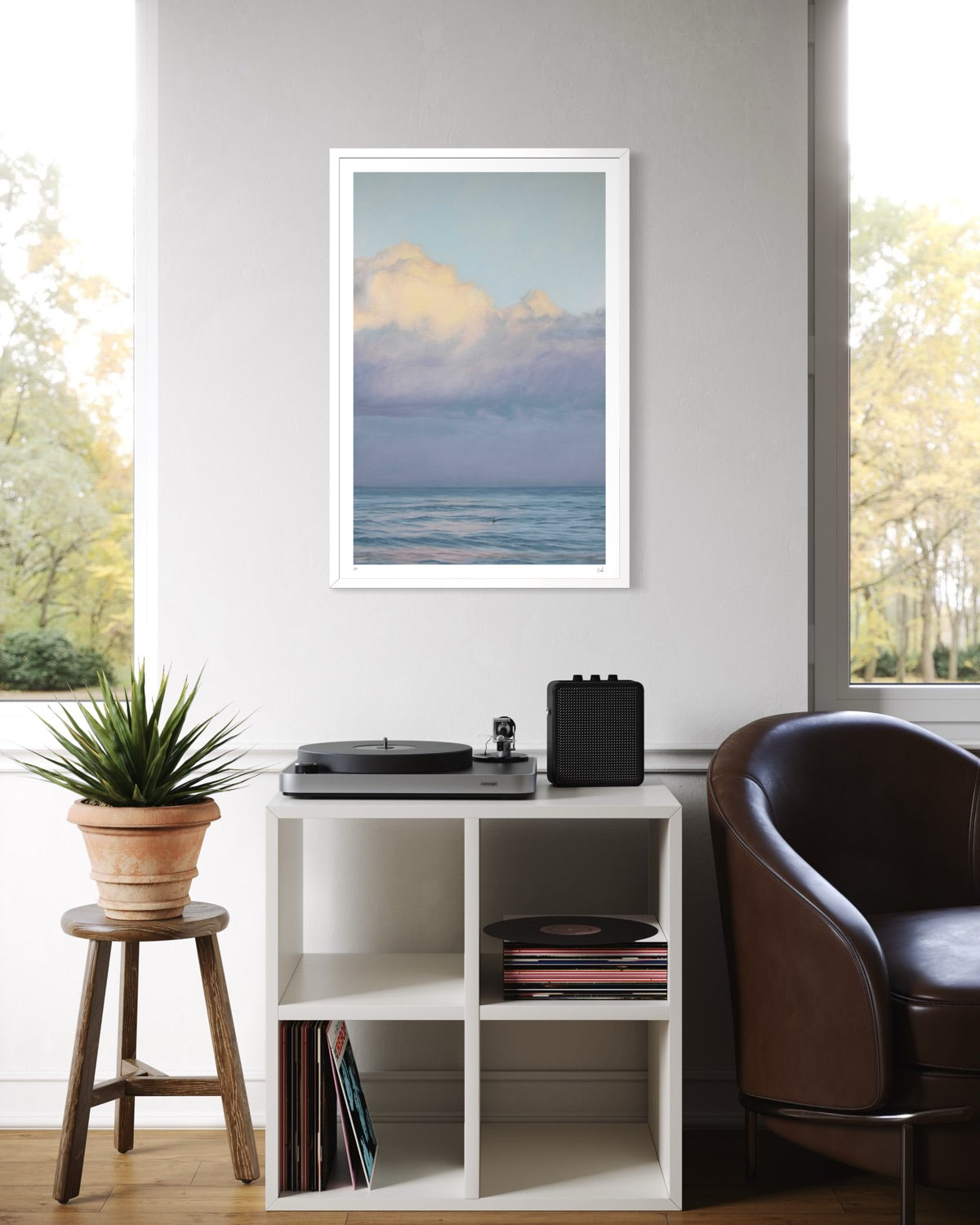 Framed artwork of a beach scene above a record player on a shelf in a room with a window and plant.