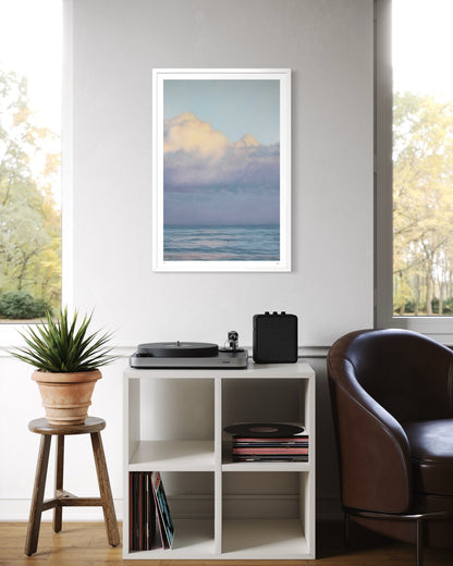 Framed artwork of a beach scene above a record player on a shelf in a room with a window and plant.