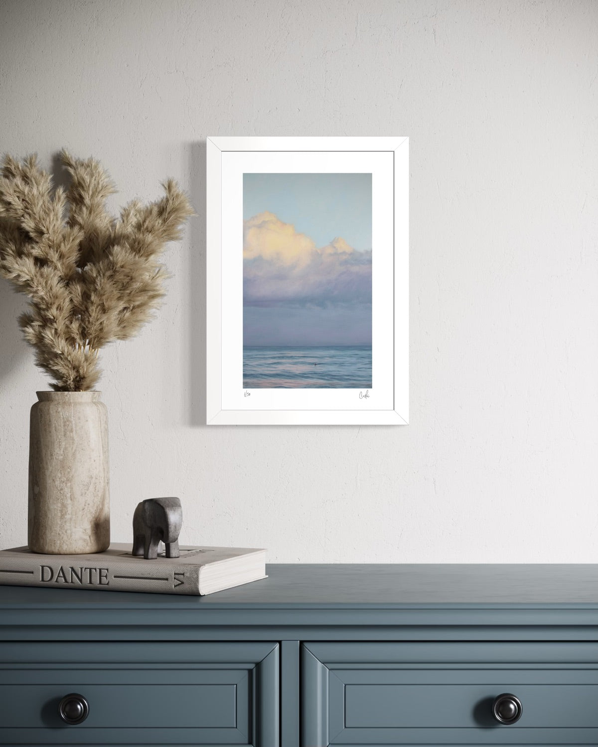 Framed artwork of a beach scene on a wall above a blue cabinet with decorative items.