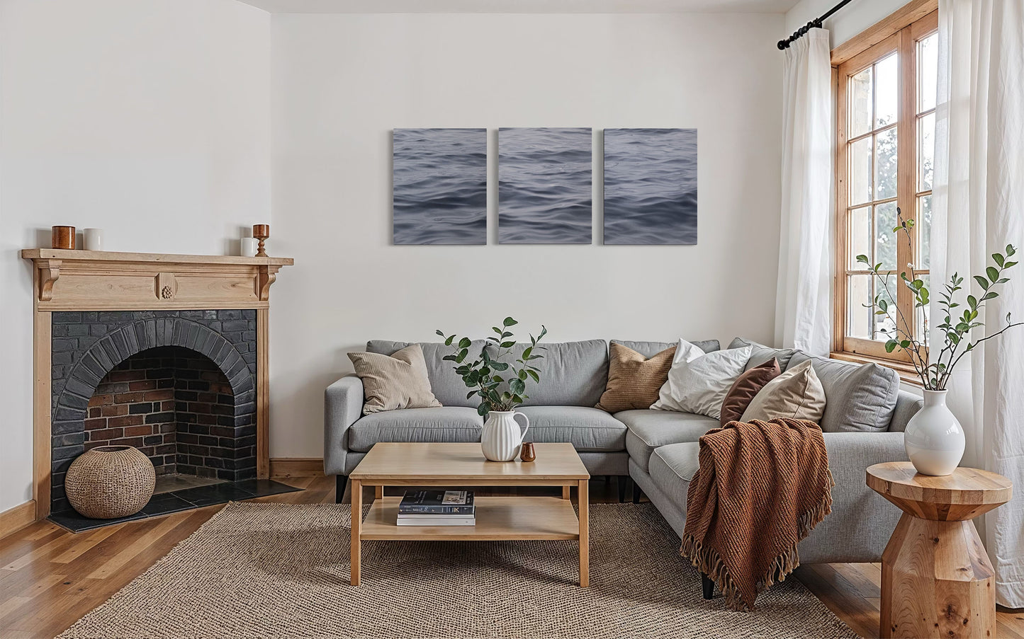Original ocean triptych wall art above gray sofa in modern coastal living room with fireplace.