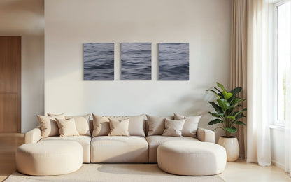 Large triptych seascape oil painting displayed above neutral sofa in bright coastal living room interior.