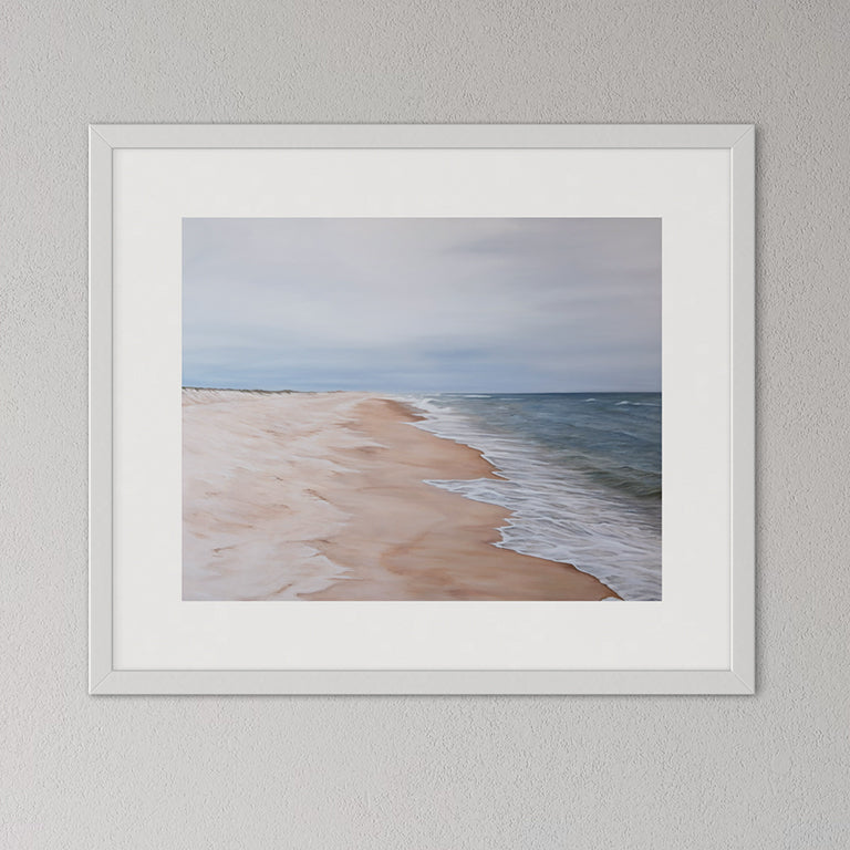 Framed artwork of a beach scene with a white frame on a gray wall.