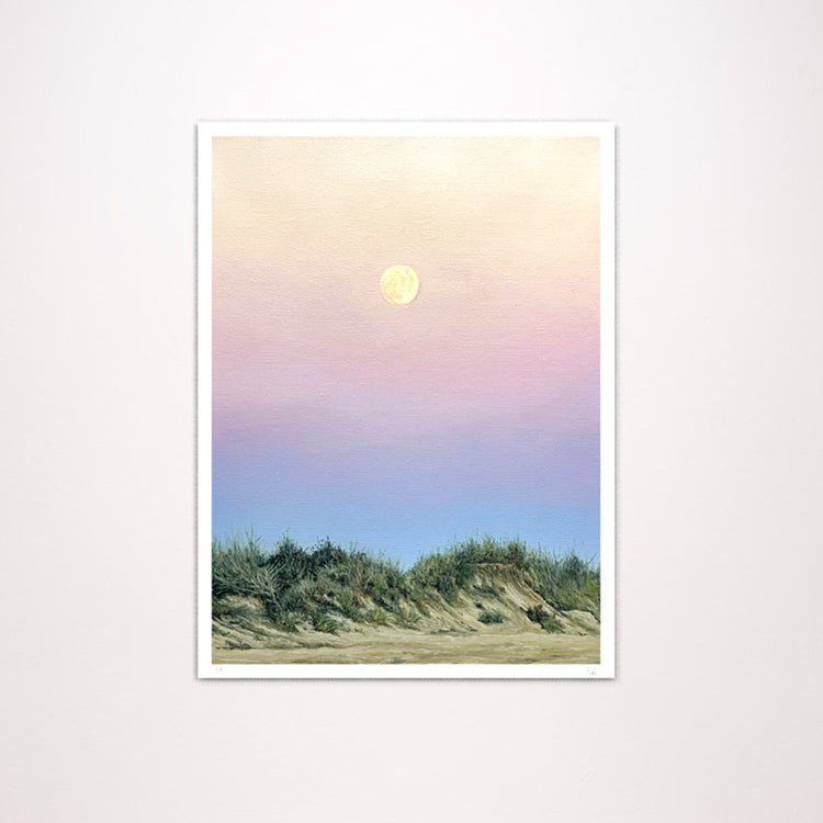 A vertical art print featuring a pastel landscape of beach dunes under a soft pink, purple, and blue sky with a glowing moon, shown against a light neutral background.