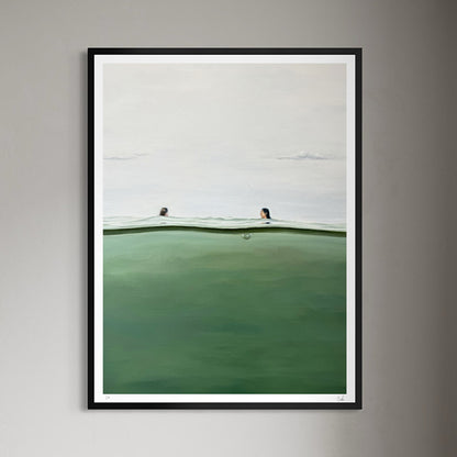 A framed art print depicting a minimalist seascape with two swimmers in a calm green ocean under a pale sky, mounted on a neutral gray wall.