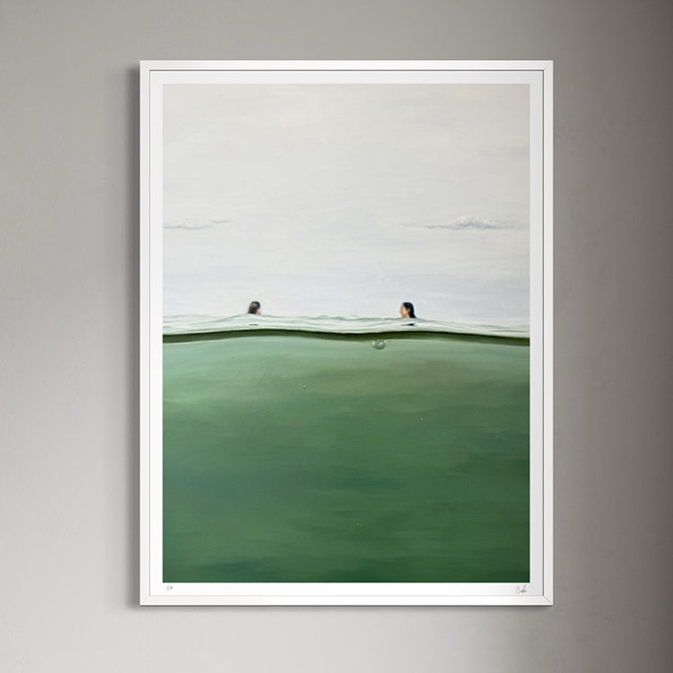 A framed art print depicting a serene landscape with two swimmers in a calm green and white body of water, hung on a neutral gray wall.