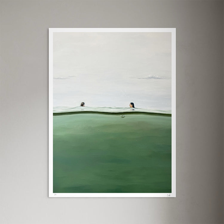 A framed art print featuring a minimalist landscape of a green-tinted body of water under a pale gray sky, with two small figures visible above the horizon. The print is displayed against a neutral gray wall.