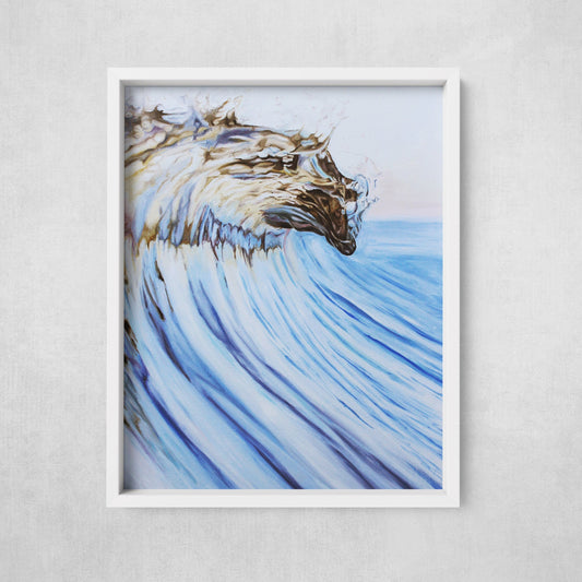 A framed fine art paper print of a curling ocean wave, with golden hues against a cooler blue background, presented against a plain wall.