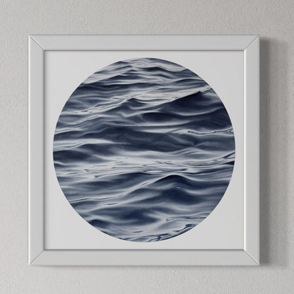 A framed fine art print of the ocean with a predominantly blue and white color palette, displayed on a wall.