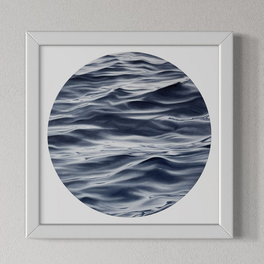 A framed fine art print of the ocean with a predominantly blue and white color palette, displayed on a wall.