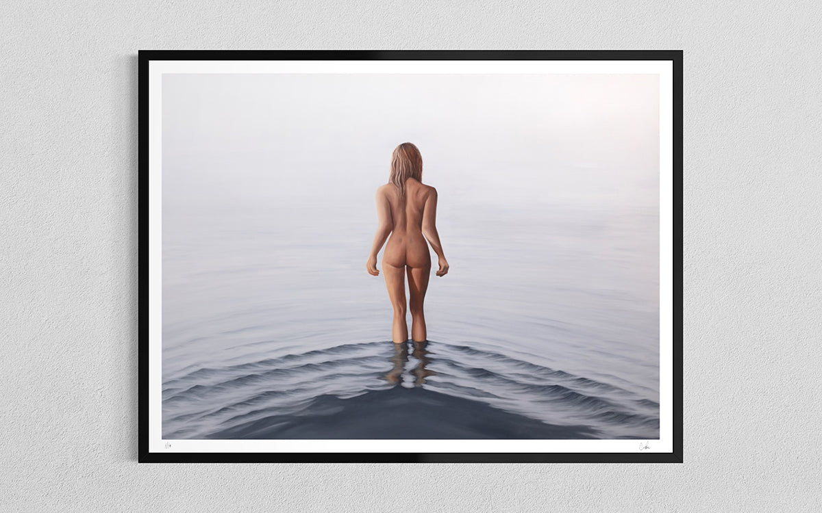 A framed oil paiting art print hanging on a light gray wall. The print shows a nude woman standing in calm water, viewed from behind, with a black frame and white mat border.