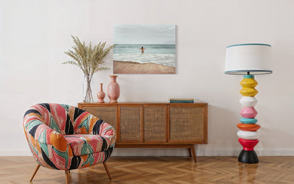 Colorful armchair in a room with a wooden sideboard, lamp, and beach-themed artwork.