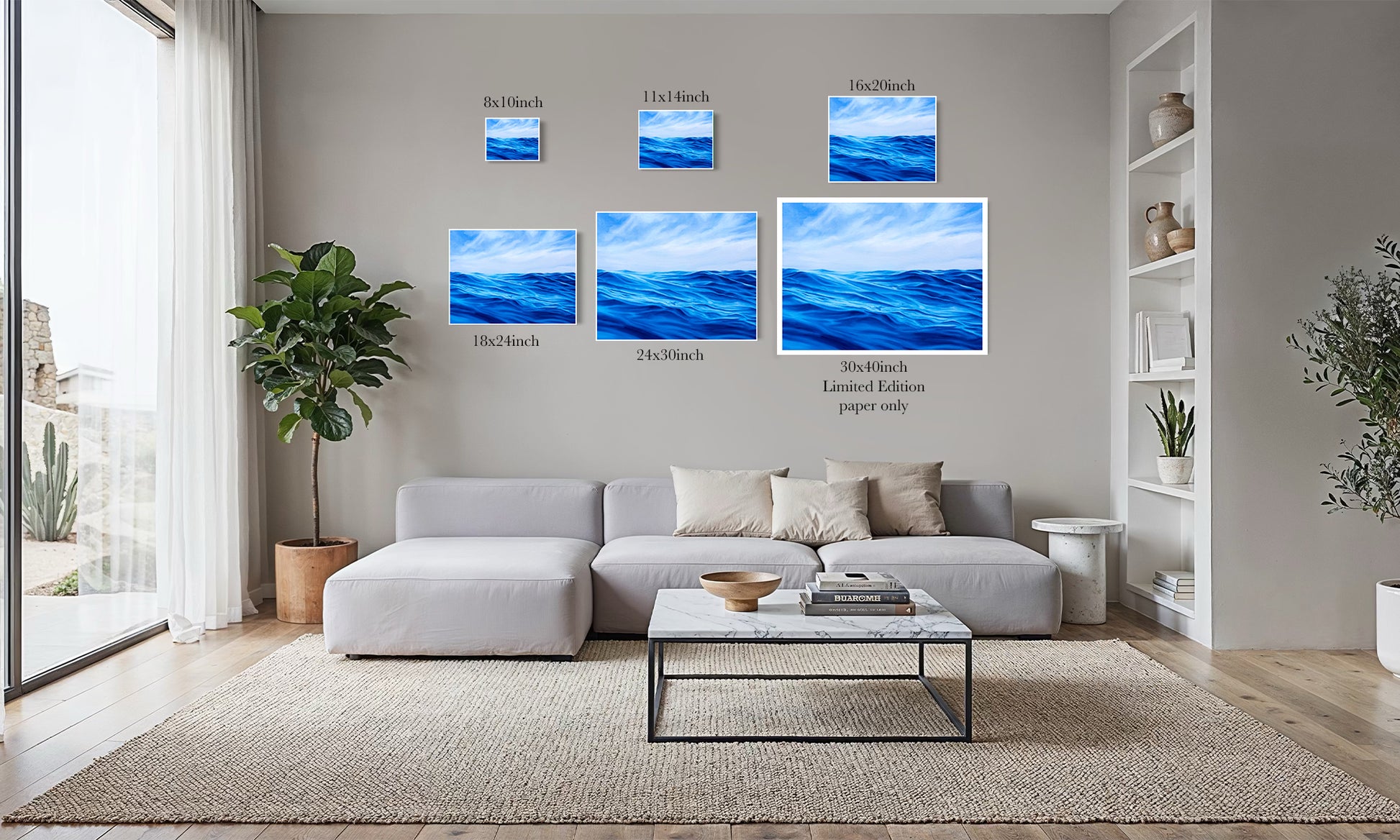 A modern living room with a light gray sectional sofa, coffee table, and wall-mounted ocean artwork in multiple sizes with printed dimensions and text labels. The room is styled with plants, shelving, and a large window.