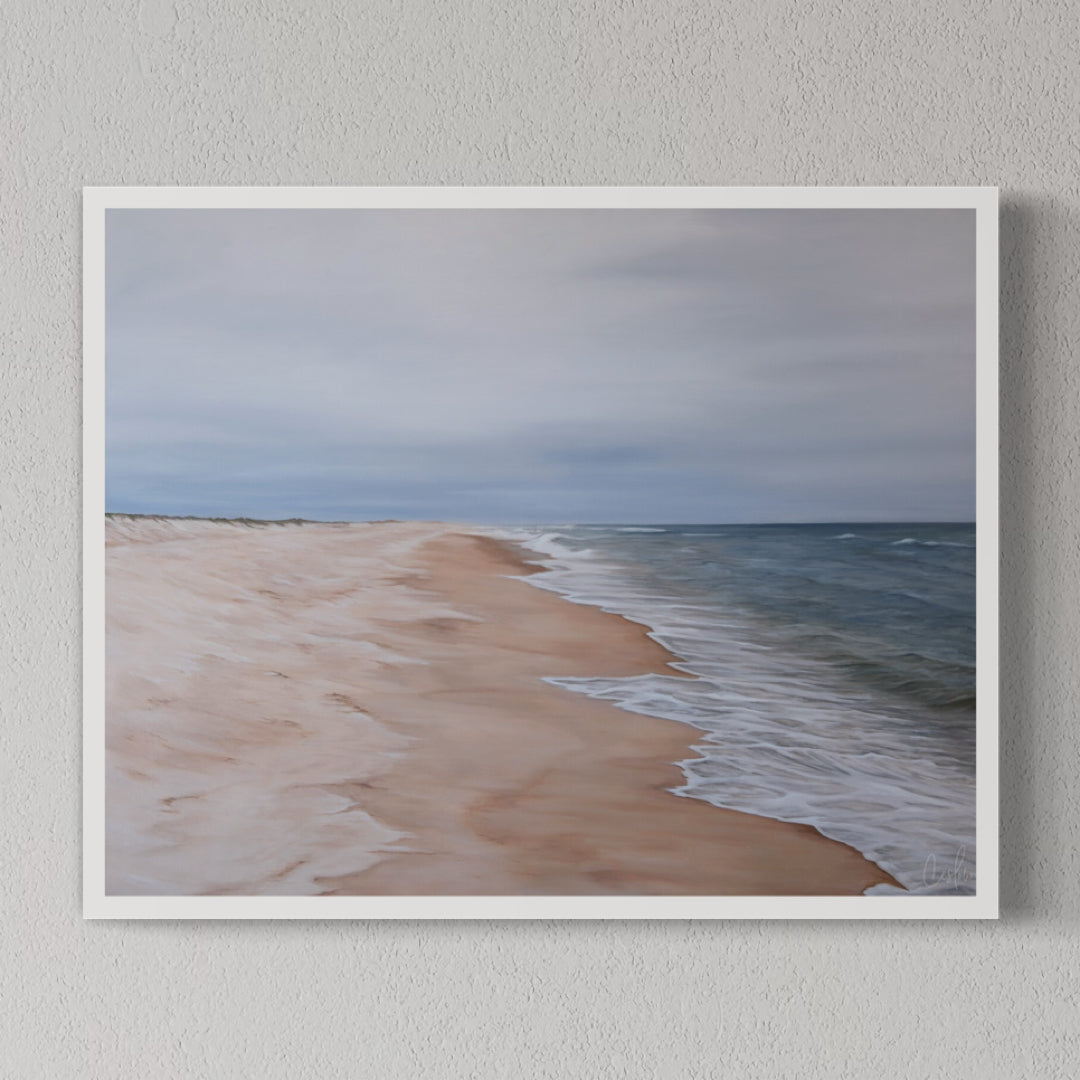 A framed print depicting a serene beach scene with gentle waves and a expansive sky, mounted on a wall.