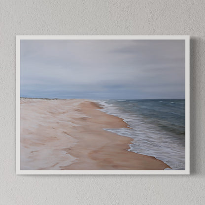 A framed print depicting a serene beach scene with gentle waves and a expansive sky, mounted on a wall.