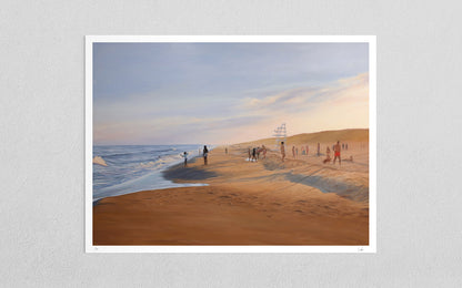 A framed art print depicting a beach scene with sand dunes, ocean waves, and small figures of people, displayed against a light gray textured wall.